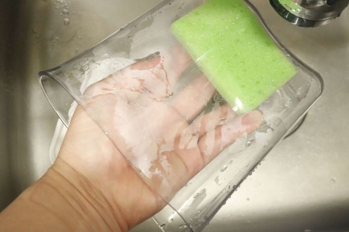 透明なピッチャーの内部を緑色のスポンジで洗っている