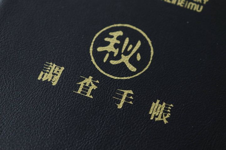 ムーのレザー調ノートの表紙に施されたゴールドの箔押し「秘」「調査手帳」の文字のクローズアップ