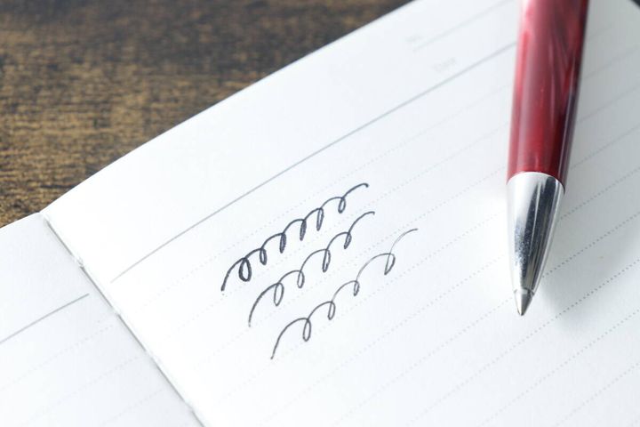 ムーのレザー調ノートに赤いボールペンで文字を試し書きしている手元のクローズアップ