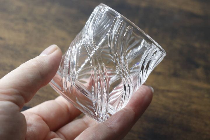 手で波模様のミニグラスを持ち、光が反射している