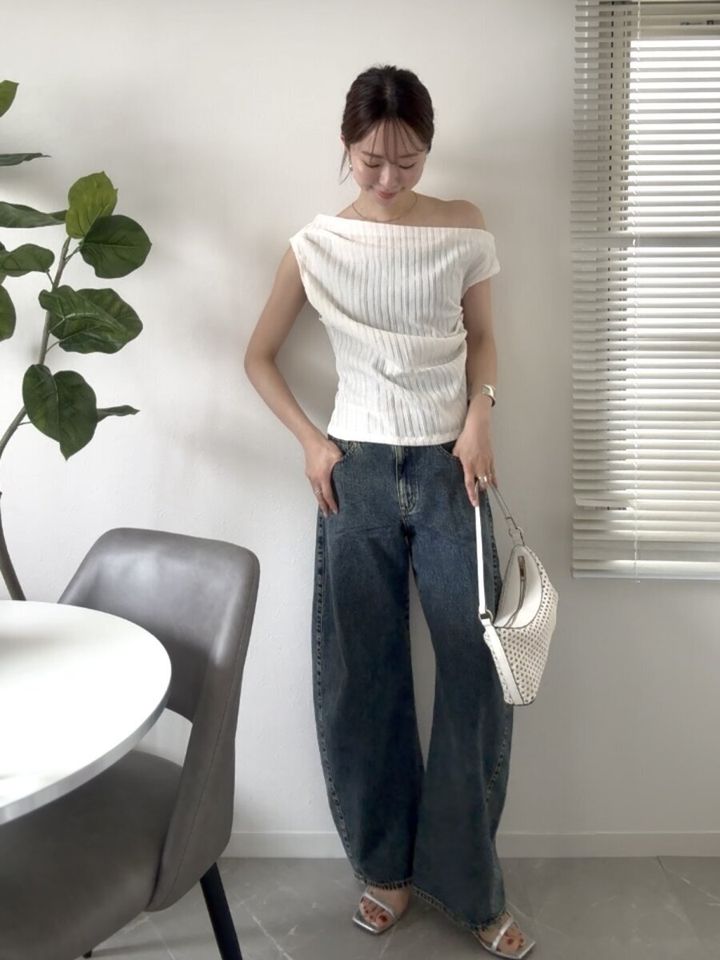 白いワンショルダートップスと3Dバレルジーンズを着た女性