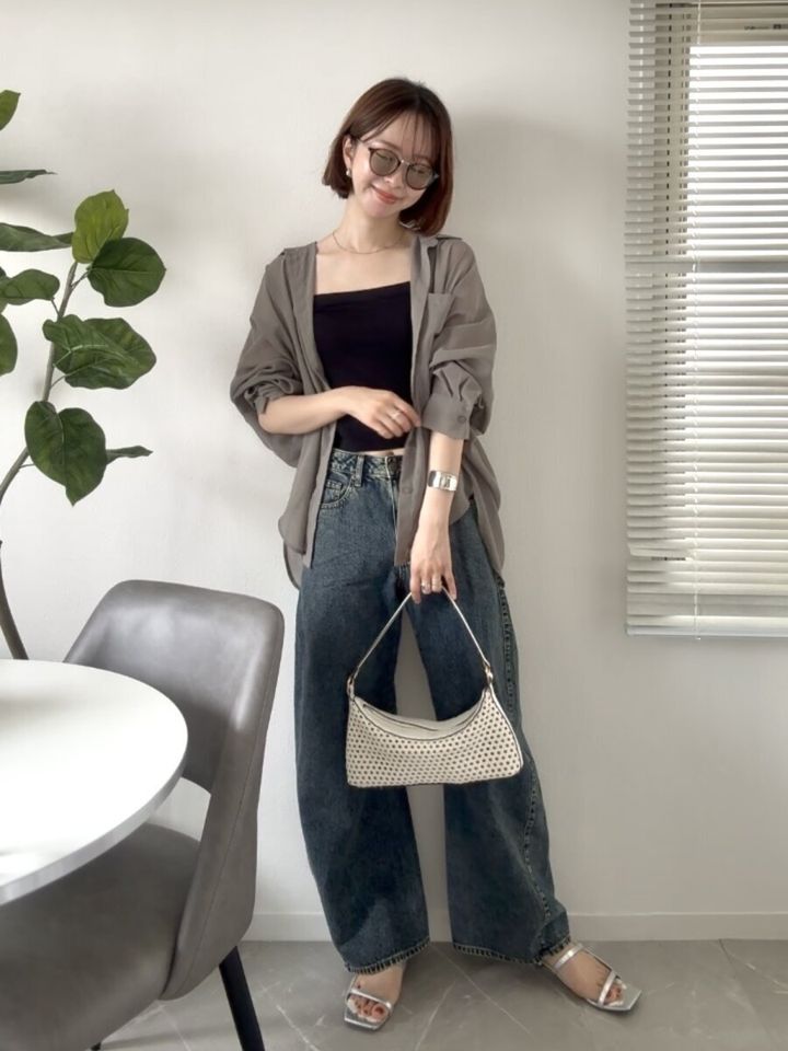 カーキのシアーシャツと3Dバレルジーンズを着て立つ女性