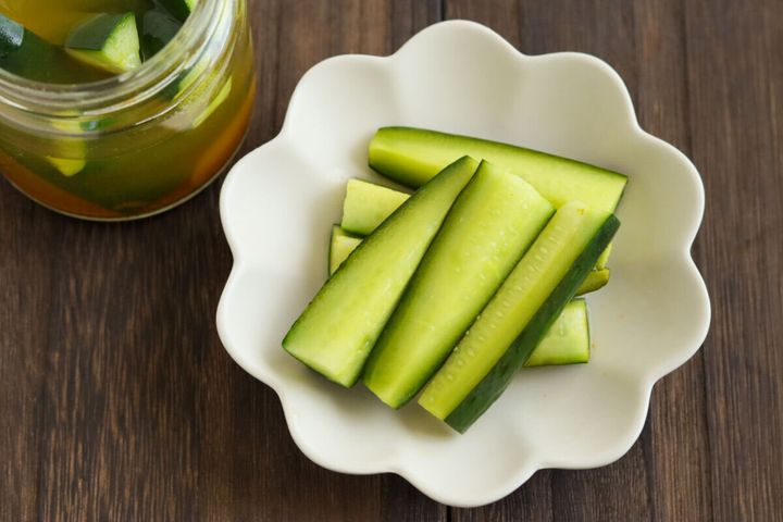 白い花形の器に盛り付けられたきゅうりのカレーピクルスと、瓶に入ったピクルス液の俯瞰