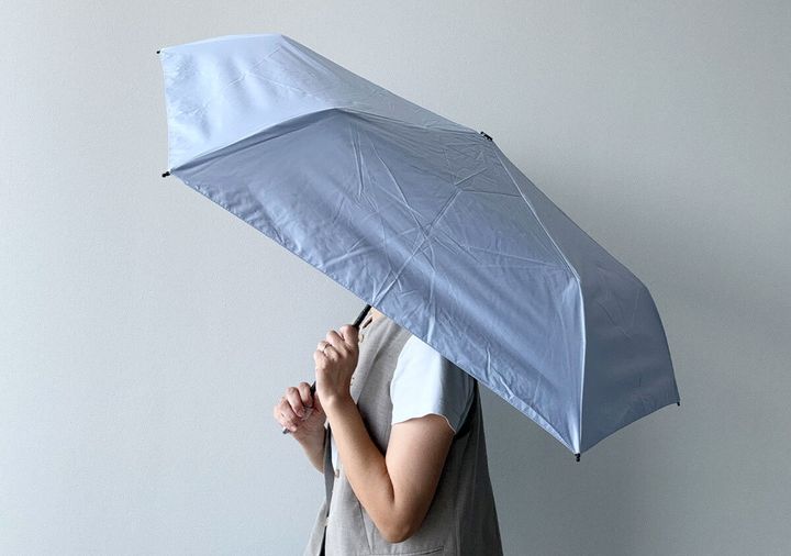 淡い紫色の折りたたみ傘を差して顔を隠している人物の横顔