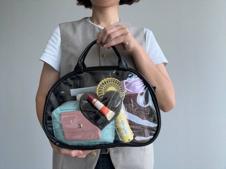女性が黒いクリアバッグを持ち、中身の小物を見せている