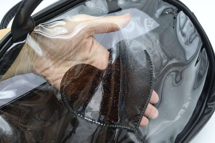 黒いクリアバッグのハート型ポケットに手を入れて物を入れている
