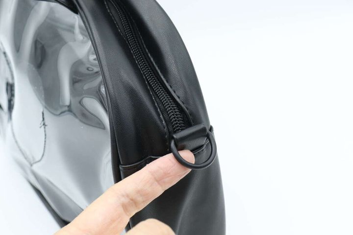 黒いクリアバッグ側面にあるショルダーストラップ用Dカンを指で示している