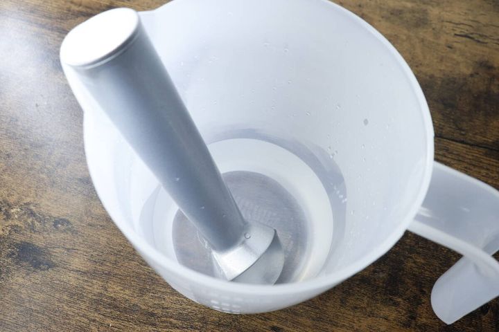 アルミ製アイスクリームスクーパーが、お湯の入った白い計量カップに入れられている