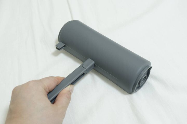 粘着テープをセットしたカーペットローラーで床を掃除する手