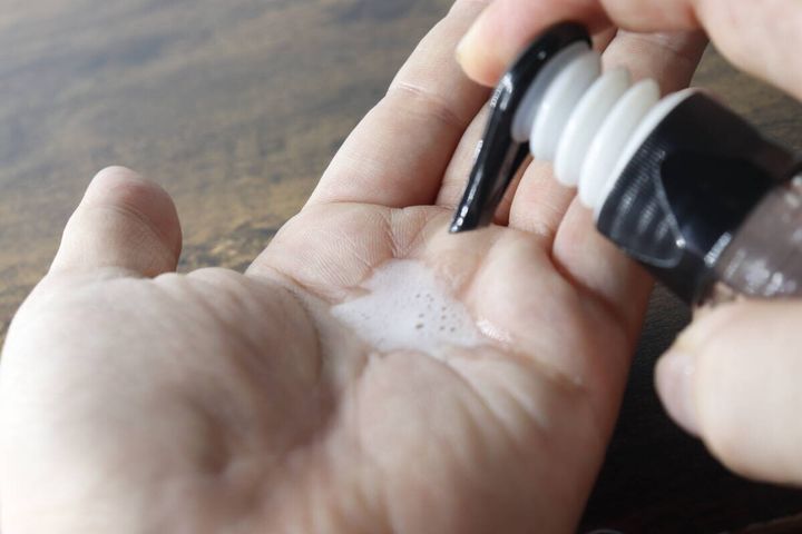ポンプボトルをプッシュして手のひらに白い泡を出している