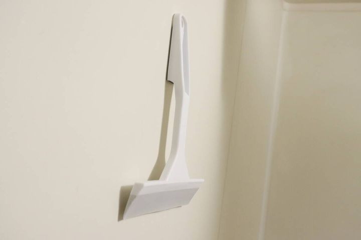 白い水切りワイパーが浴室の壁にマグネットで貼り付けられて収納されている様子