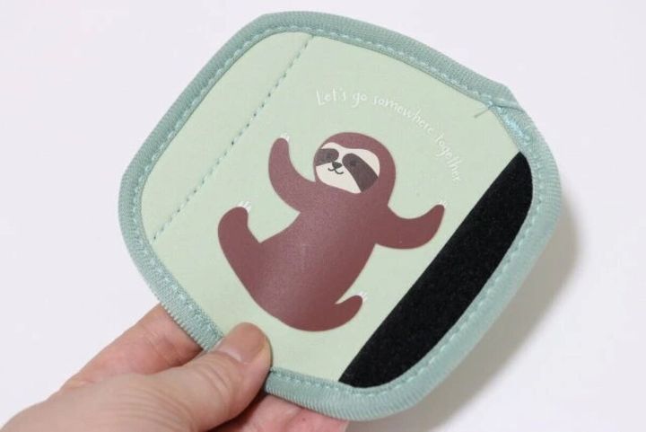 ナマケモノが描かれた緑色のスーツケースハンドルカバーを、右手が広げて持っている