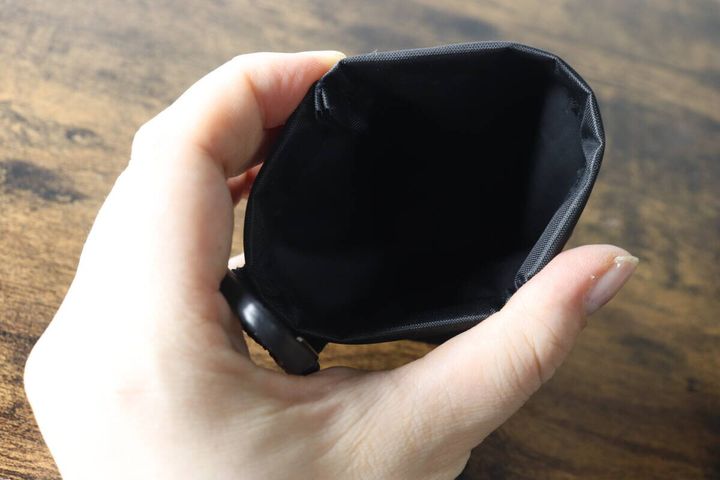 女性の手が黒い携帯ごみポーチのバネ口を開き、内側が見えている