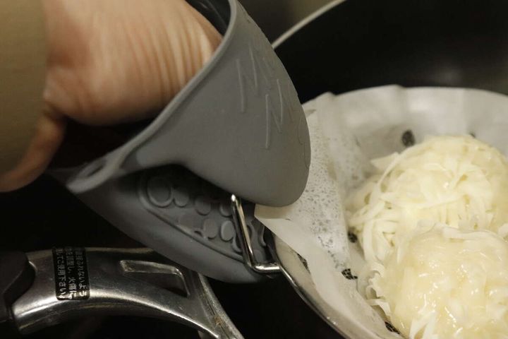ミトンを使いフライパンから浅型ザルを持ち上げている手元