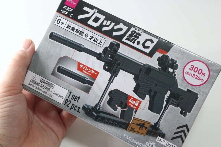 手に持ったダイソーのブロック銃パッケージ。サイレンサーや引き金の表示。