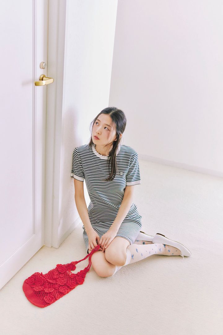 ボーダーのミニワンピースに小花柄ソックスと白シューズを合わせ、赤いメッシュバッグを手元に置いて佇む片山友希のフレンチレトロなコーディネートカット