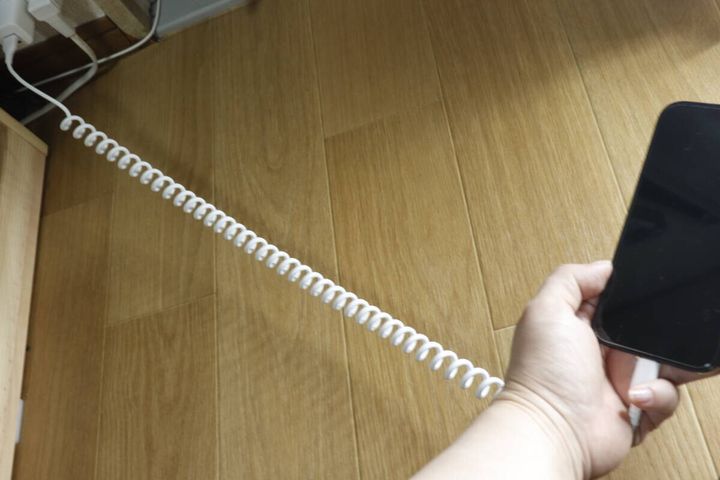床に伸びた白いコイルケーブルでスマホを充電している手元