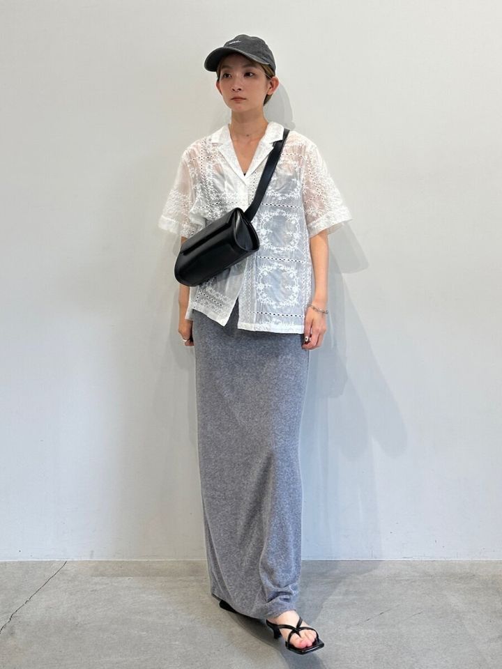 白いレースシャツとグレーのIラインスカートを着た女性が黒いキャップとバッグを身につけている