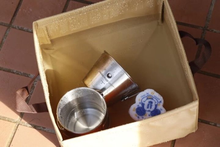 ベージュのキャンプバケツに水と食器、スポンジが入っている