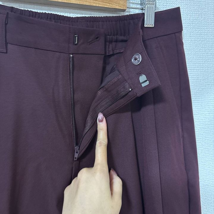 女性がワイン色のタックワイドパンツのファスナーとホックを指す