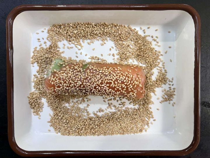 白いりごまを敷き詰めたバットの中で、生春巻きにごまをまぶしている工程の写真