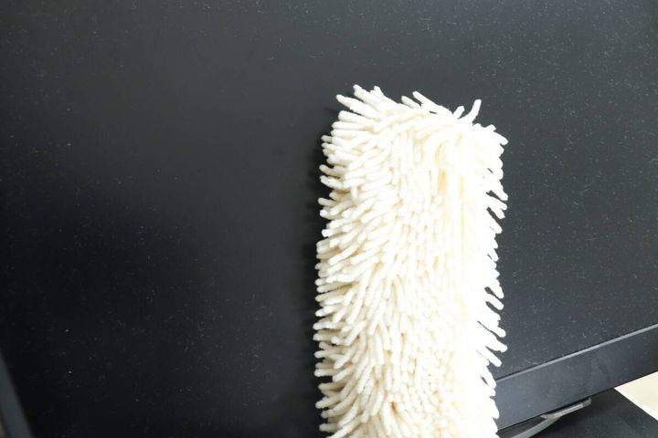 黒いモニター画面のホコリを白いハンディモップで拭いている様子