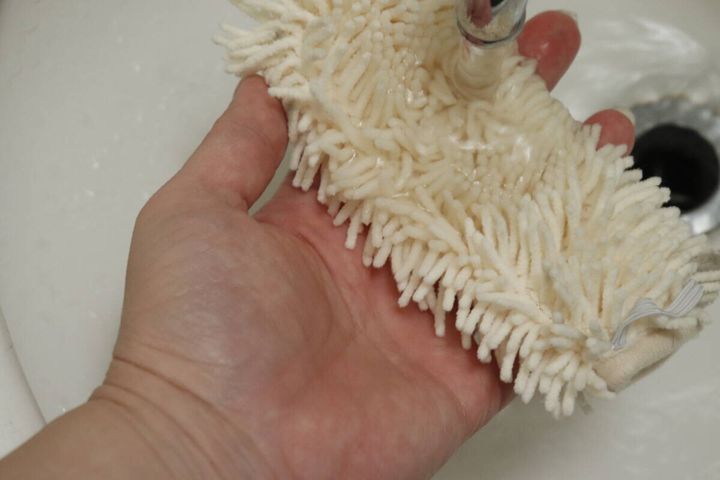 流水で白いハンディモップの汚れを洗い流している手元