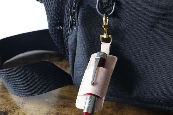 赤いペンを差したペンホルダーを黒いバッグに吊り下げている