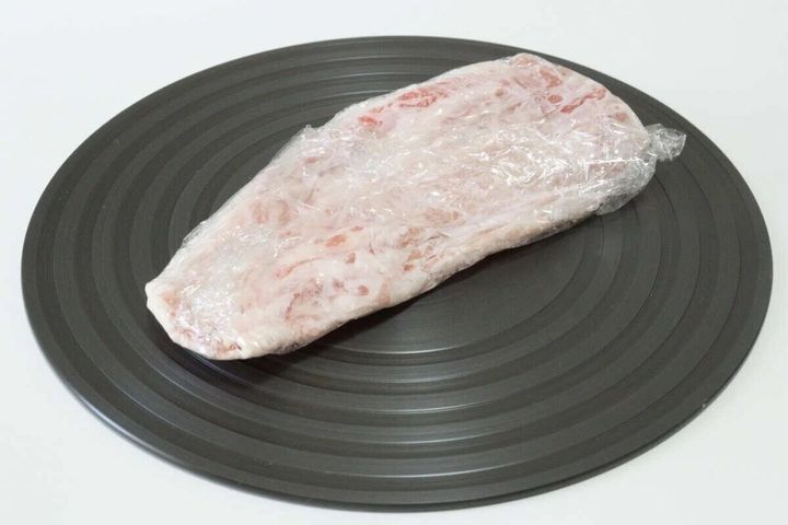 黒い円形の解凍プレートにラップされた冷凍肉が乗っている