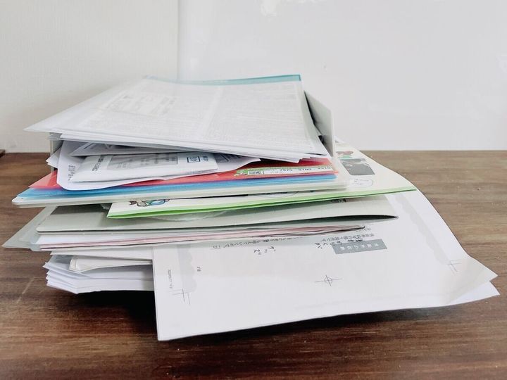 木目のテーブルに積み重なった大量の書類と封筒
