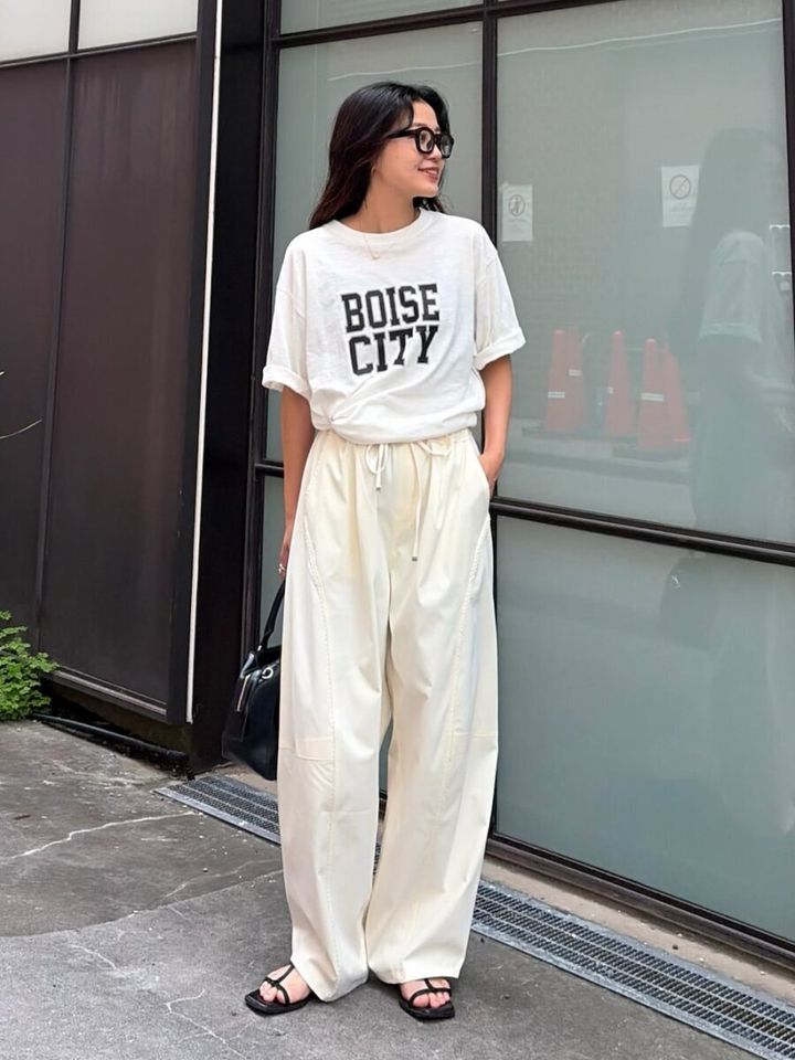 黒縁メガネの女性が白Tシャツと白バレルパンツで立つ全身