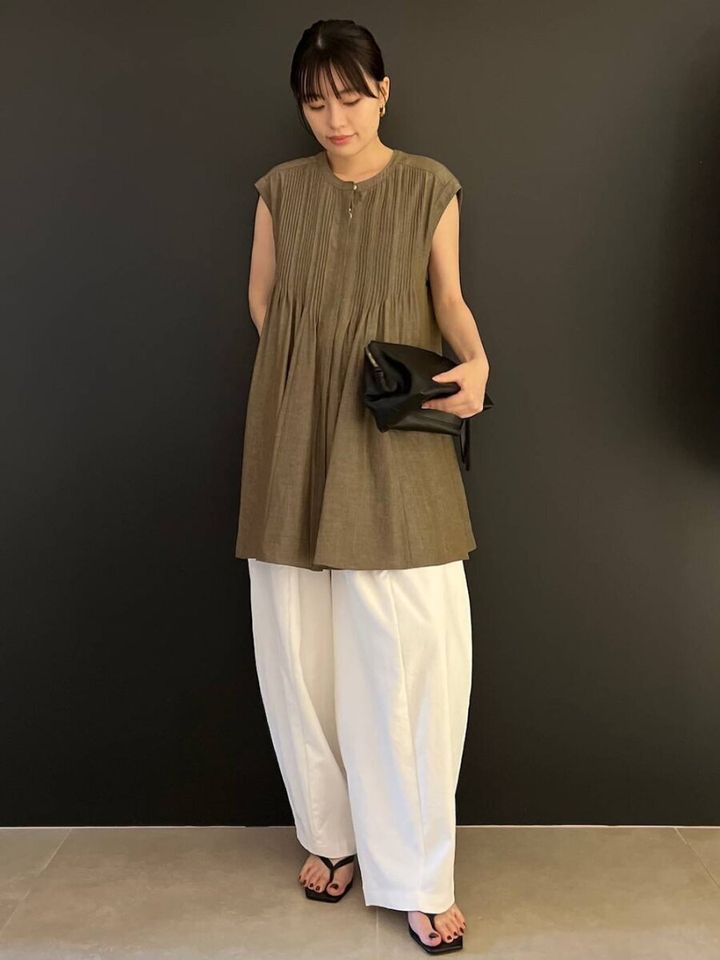 カーキブラウスと白バレルパンツ姿の女性が立つ