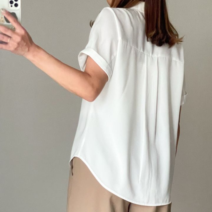 白い半袖シャツとベージュパンツの女性の後ろ姿がスマホで自撮り