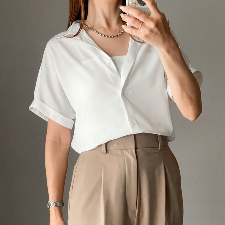 白い半袖シャツとベージュパンツの女性がスマホで自撮りしている