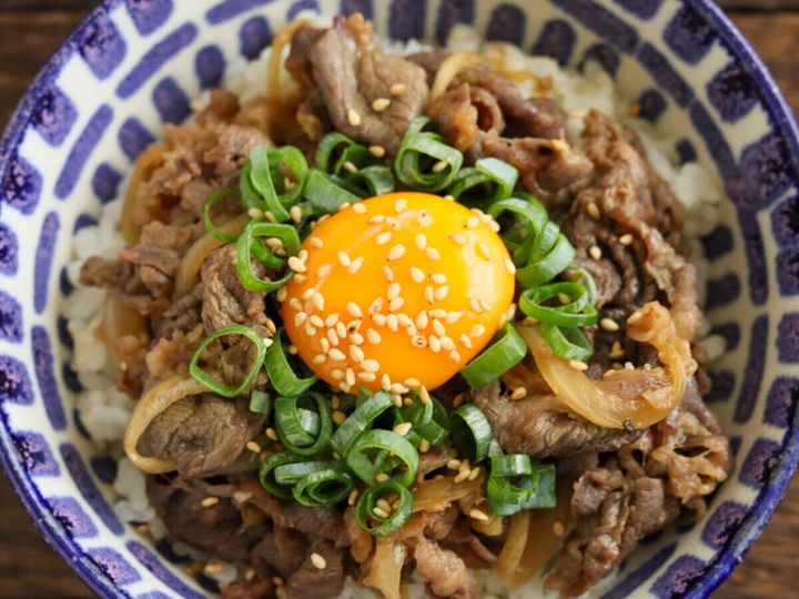 模様の丼にご飯と炒めた牛肉、卵黄、小ねぎ、白いりごまが盛られたスタミナ丼の俯瞰
