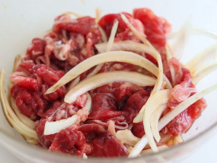 透明なガラスボウルに牛切り落とし肉と薄切り玉ねぎが入っている