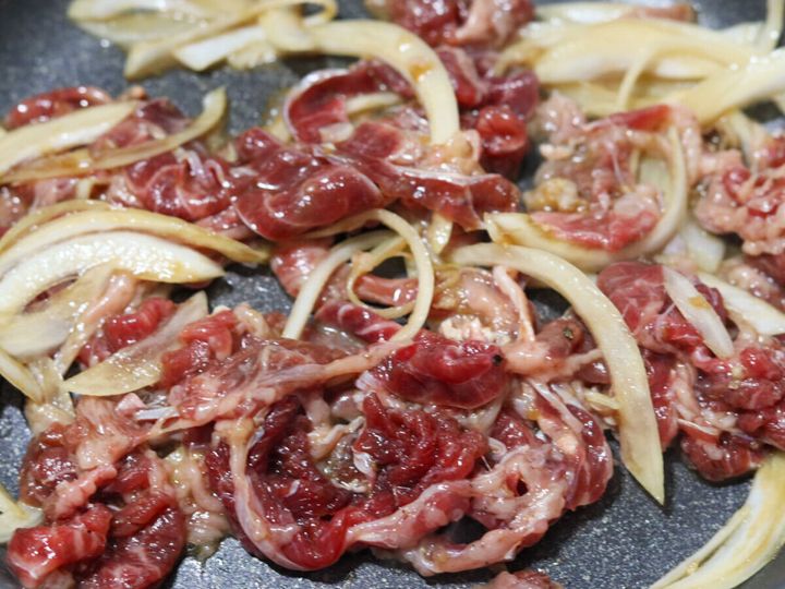 フライパンで漬け込んだ牛肉と玉ねぎをごま油で炒め始めた様子