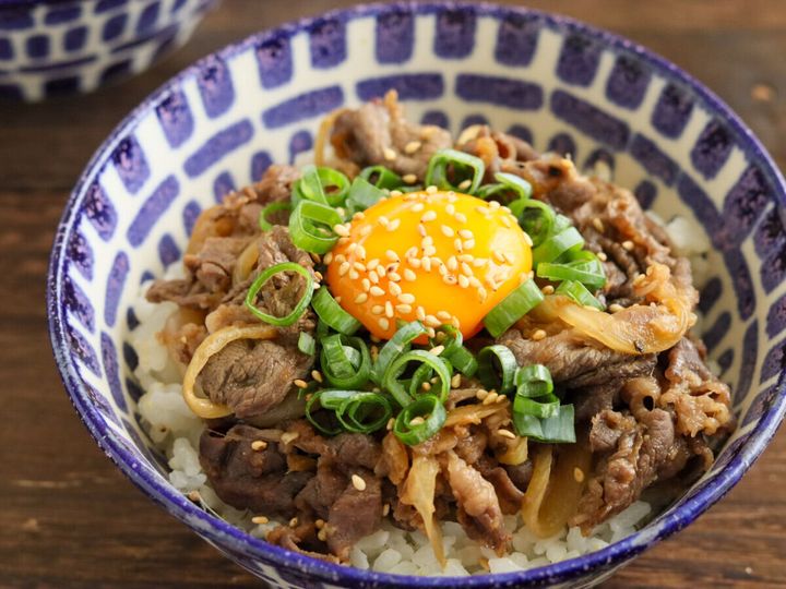 模様の丼にご飯と炒めた牛肉、卵黄、小ねぎ、白いりごまが盛られたスタミナ丼