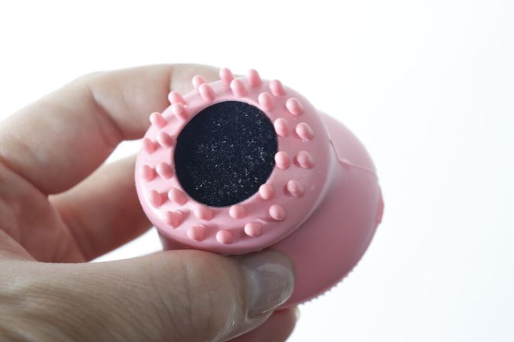 女性の手に持たれた洗顔ブラシの底面。黒いスポンジと突起が見える