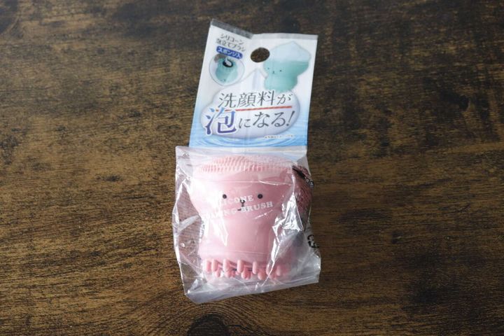 パッケージに入ったピンク色の洗顔ブラシが木目のテーブルに置かれている