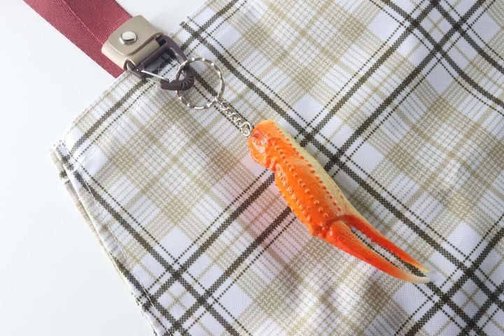 チェック柄のバッグの持ち手に取り付けたバッグキーベルトに、カニの爪のキーホルダーがぶら下がっている。