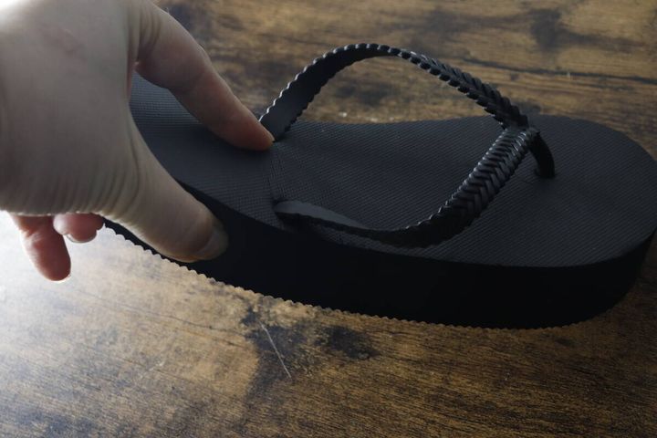 指で黒い厚底ビーチサンダルのソール部分を押して弾力を確認している