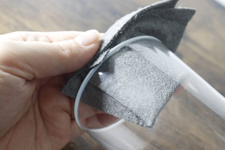 グレーのクロスで透明なグラスの縁を拭いている手元