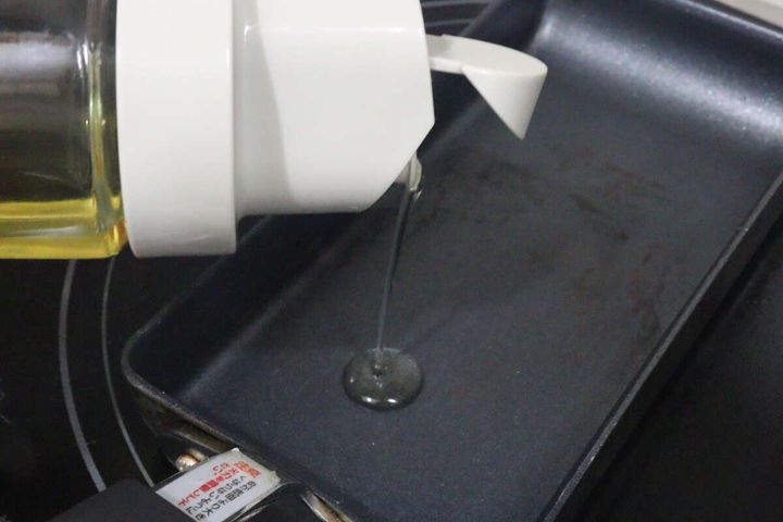 オイルボトルからフライパンに食用油を注いでいる様子