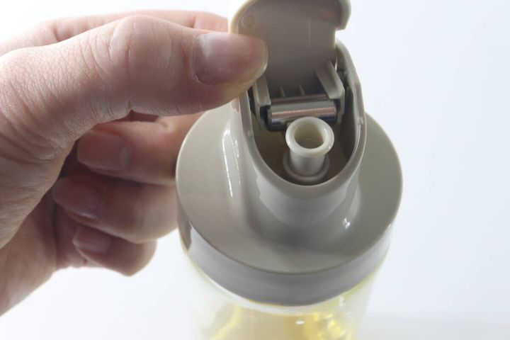 オイルボトルの蓋を開け、液だれがないか確認している手のアップ