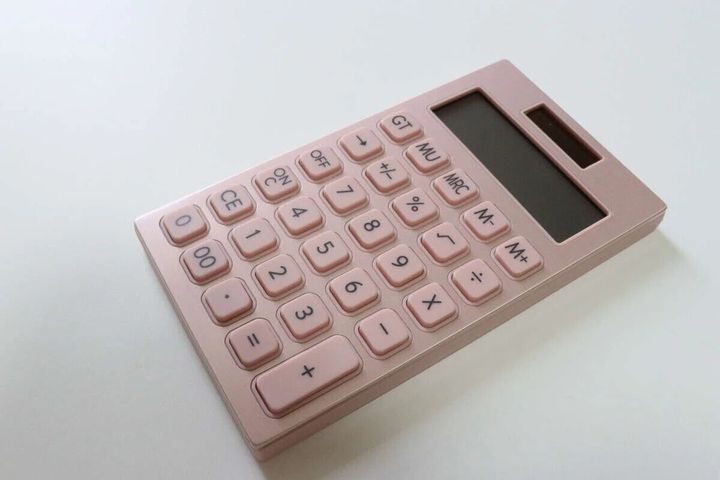 ピンクゴールドのアルミボディのおしゃれな電卓が白い机の上に置かれている。