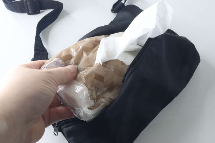 手が茶色いソフトパックティッシュをバッグの背面ポケットに入れている