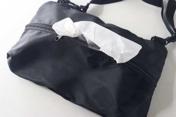 黒いショルダーバッグの背面ポケットから白いティッシュが出ている