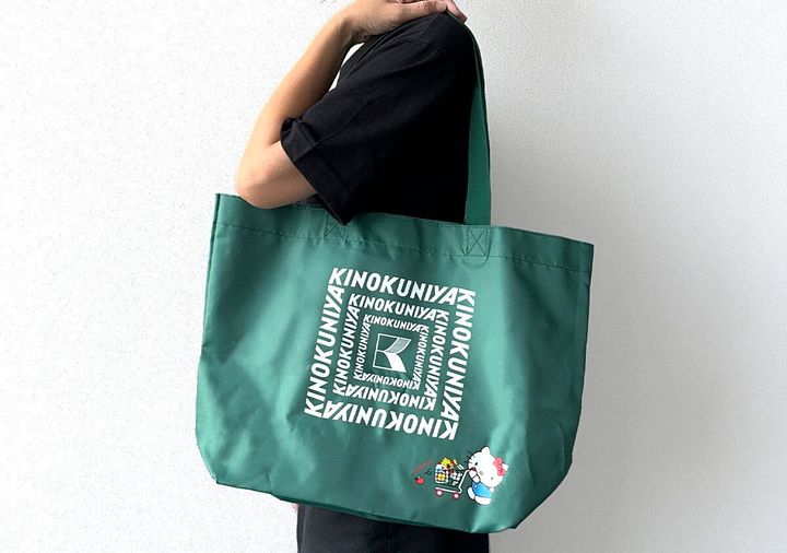 黒い服を着た人が緑色の紀ノ国屋×ハローキティお買い物バッグを肩にかけている