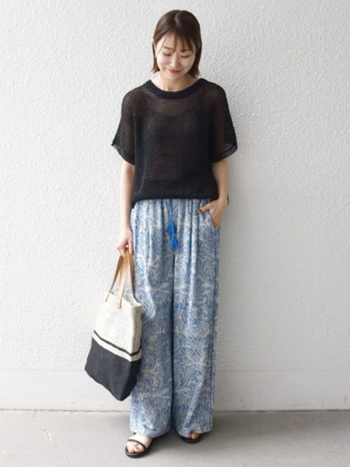 透け感黒ニットと青柄ワイドパンツ、トートバッグを持った女性